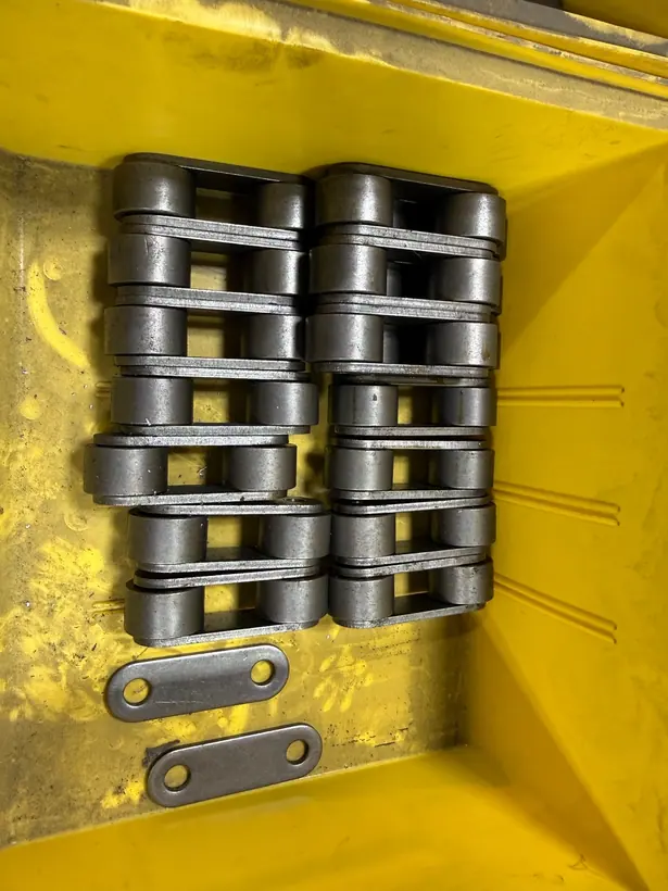 Machined chain links stacked in two rows beside two flat belt links, viewed from above.