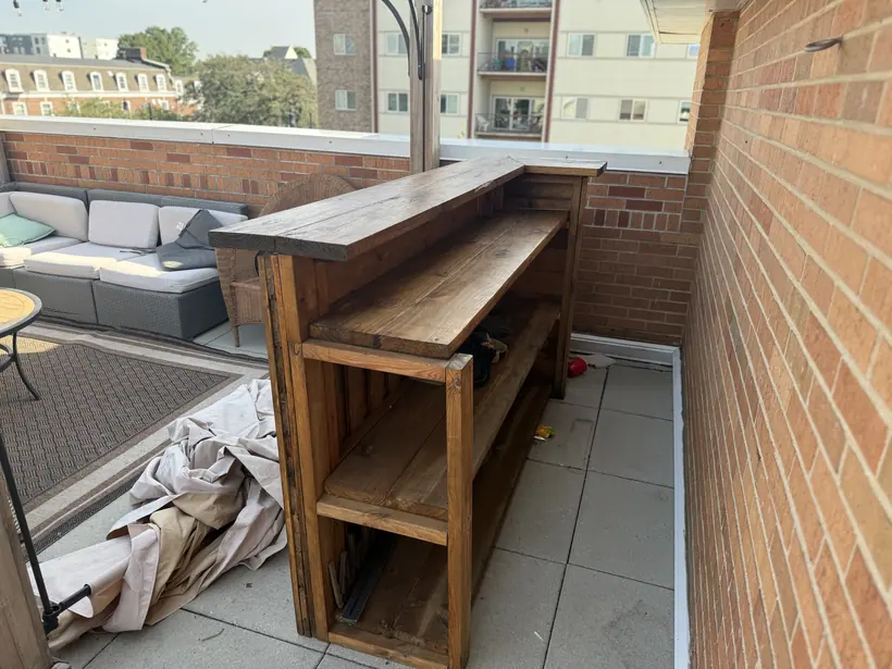 The finished structure from the work side, showing the stained timber shelves, the vertical end frame, and the overhanging bar top.