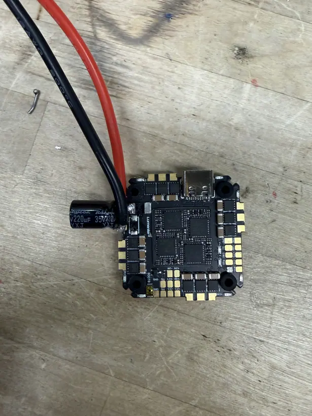 The flight-control board on its own, off the frame, with a thick red and black battery lead and a cylindrical 35 V 220 microfarad electrolytic capacitor soldered to the power pads at one edge.