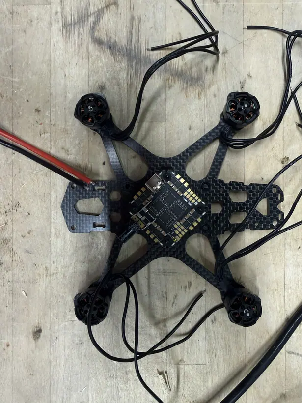 Closer overhead view of the same stage: a brushless motor at each arm tip of the carbon-fiber frame, the flight-control board at the center, and each motor's three black phase leads still loose and untrimmed.