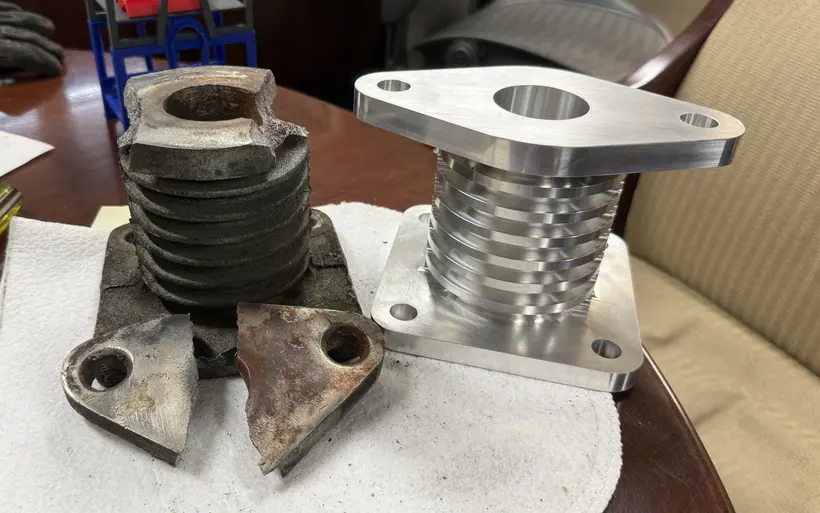 Broken furnace component beside its newly machined replacement, with the fractured flange pieces in front.